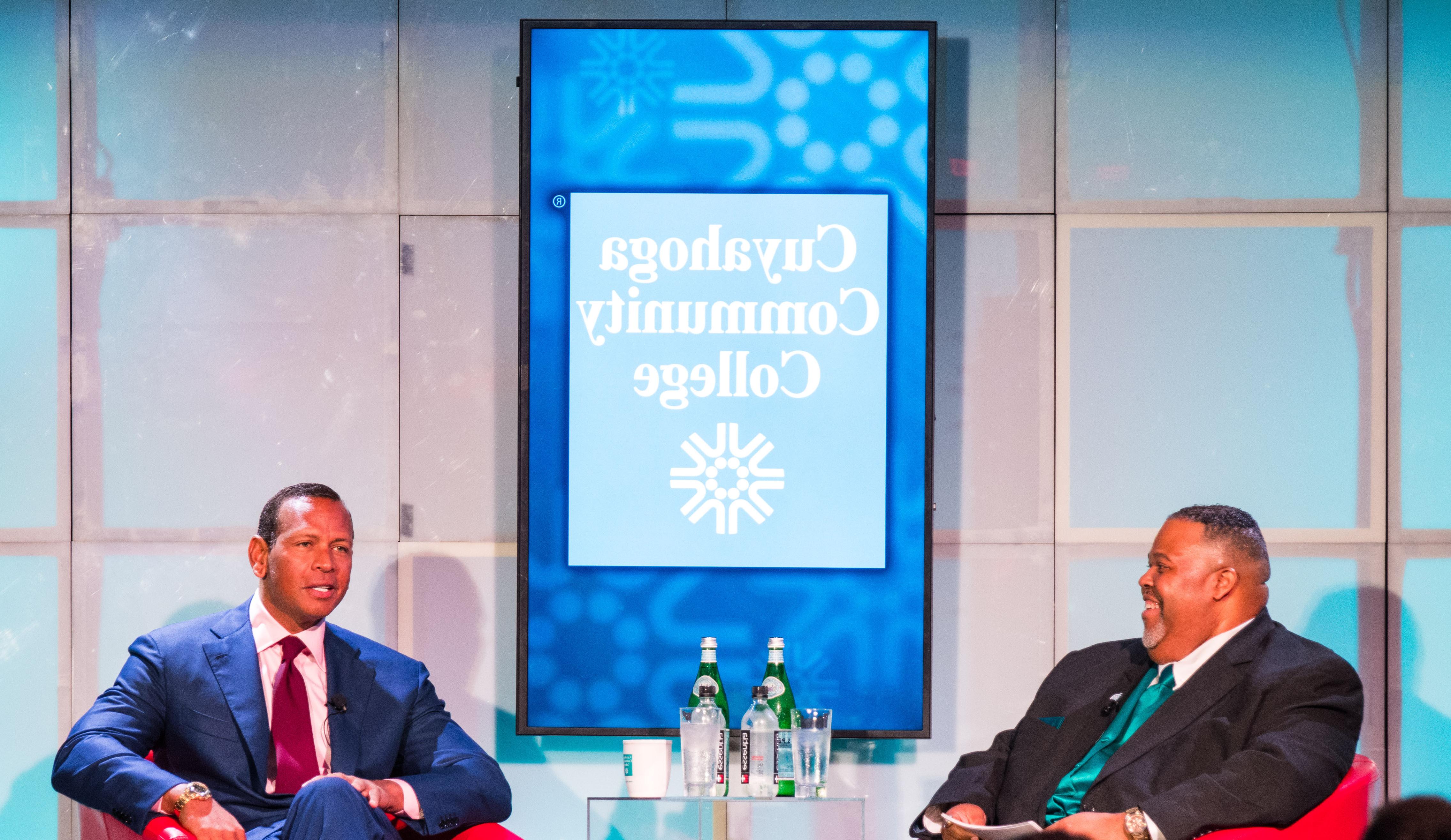 Tri-C President Dr. Michael Baston in conversation with Alex Rodriquez. Seated on stage in red club chairs under the Cuyahoga Community College logo and signage 